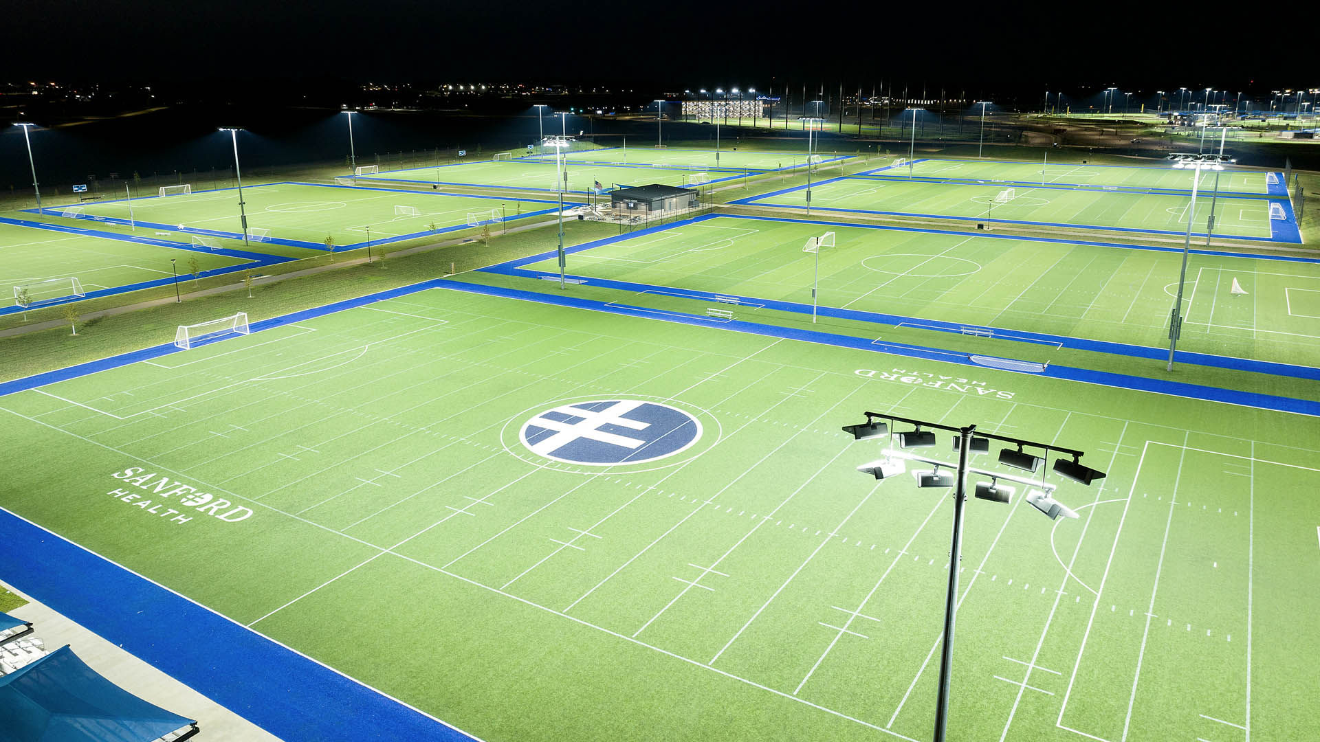 Eight soccer/multipurpose fields with blue Sanford Sports Complex logo in the center and new Musco LED sports lighting fixture in the foreground.